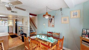 A dining area with a glass table, wooden chairs, a ceiling fan, and a staircase. - Cinnamon Teal 10 (Ocean City)