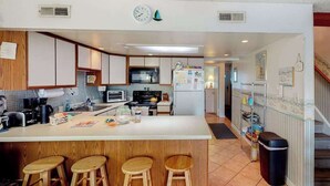 A modern kitchen with a central island, wooden stools, a microwave, stove, and a refrigerator. - Cinnamon Teal 10 (Ocean City)