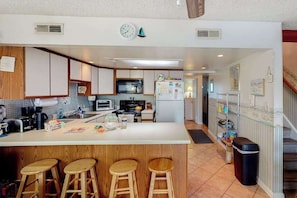 A modern kitchen with a central island, wooden stools, a microwave, stove, and a refrigerator. - Comfy, Oceanside Townhouse w/Private Washer/Dryer, Free WiFi, & Balcony (Ocean City)
