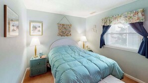 A bedroom with a bed, two bedside tables, a wall hanging, and a window with curtains. - Cinnamon Teal 10 (Ocean City)