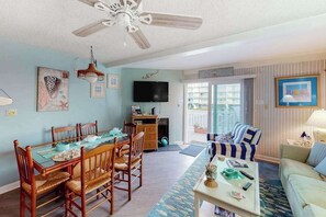 A living room with a dining table, chairs, a sofa, a coffee table, a ceiling fan, a TV, and a view through a sliding door. - Comfy, Oceanside Townhouse w/Private Washer/Dryer, Free WiFi, & Balcony (Ocean City)