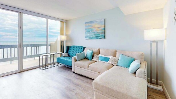 A living room with a large window, a sofa, a lamp, and a painting. - Beautiful Condo in Oceanfront Location w/Shared Pool, Free WiFi, Balcony (Ocean City)