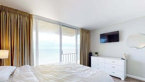 A hotel room with a bed, a dresser, a TV, and a large window with curtains. - Beautiful Condo in Oceanfront Location w/Shared Pool, Free WiFi, Balcony (Ocean City)
