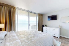 Ein Hotelzimmer mit einem Bett, einem Schminktisch, einem Fernseher und einem großen Fenster mit Vorhängen.