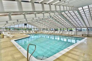 Ein hallenbad mit hoher Decke, großen Glaswänden und sonnendurchfluteten Liegebereichen.