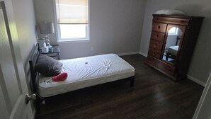 A bedroom with a single bed, a dresser, a ceiling fan, and a window with blinds.