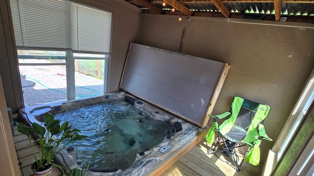 A hot tub with a wooden deck, potted plants, and a view of the outdoors.