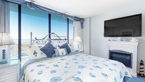 Een slaapkamer met een bed, een televisie, een open haard en grote ramen met uitzicht.