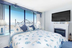 A bedroom with a bed, a television, a fireplace, and large windows with a view. - Attractive oceanfront condo with sunset views, two balconies, pool & Central AC (Ocean City)