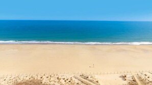 Een breed zandstrand met zachte golven, een heldere lucht en een verre horizon.