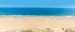 A wide sandy beach with gentle waves, a clear sky, and a distant horizon. - Attractive oceanfront condo with sunset views, two balconies, pool & Central AC (Ocean City)
