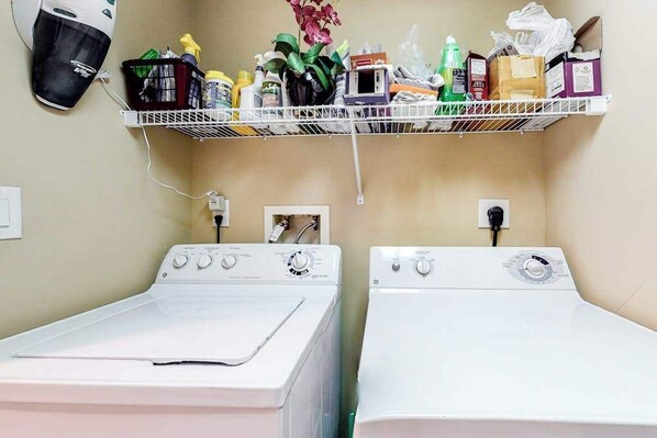 A laundry room with two washing machines, a shelf with cleaning supplies, and a power outlet. - Coral Seas 201 (Ocean City)