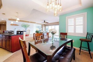 A modern kitchen with a dining area, a ceiling fan, and a large window with blinds. - Coral Seas 201 (Ocean City)