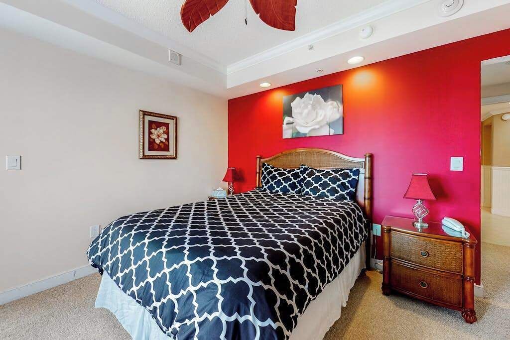 Ein Schlafzimmer mit Bett, Nachttisch, einer roten Akzentwand und einem gerahmten Bild.