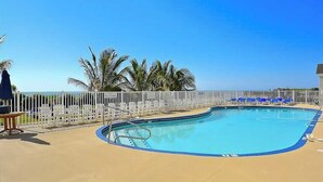 A swimming pool with a white fence, palm trees, and a clear blue sky. - Carousel 1707 (Ocean City)