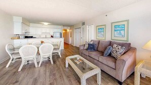 A living room with a sofa, coffee table, and dining area with chairs. - Carousel 1707 (Ocean City)
