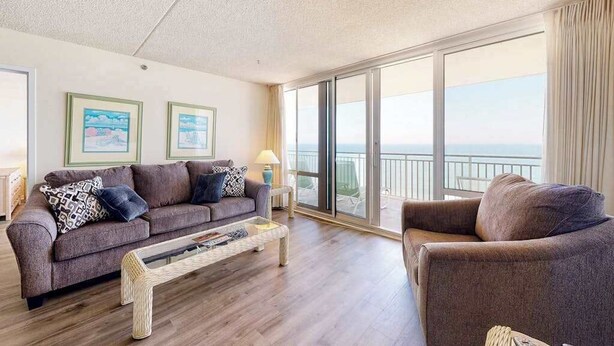 A living room with a sofa, armchair, and coffee table, large windows with a view, and framed pictures on the wall. - Carousel 1707 (Ocean City)