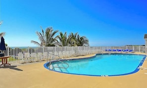 A swimming pool with a white fence, palm trees, and a clear blue sky. - Beachfront Condo with balcony, views, shared pools, gym, & sauna (Ocean City)