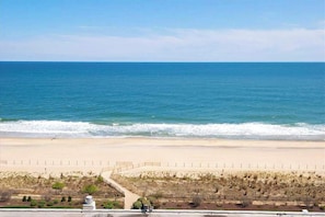 A coastal view with a beach, a road, and a fenced area with sparse vegetation. - Beachfront Condo with balcony, views, shared pools, gym, & sauna (Ocean City)
