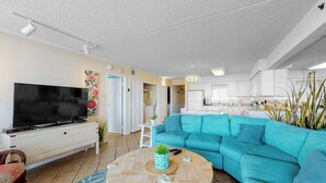 A living room with a television, a sofa, a coffee table, and a kitchen in the background.