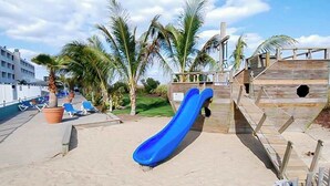 A beachside area with a blue slide, palm trees, and lounge chairs.
