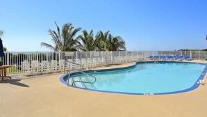 A pool with a white fence, palm trees, and lounge chairs.