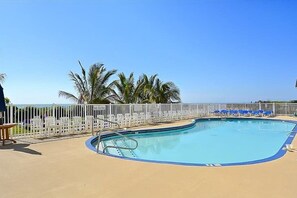 A pool with a white fence, palm trees, and lounge chairs.
