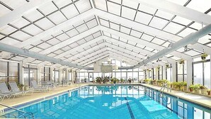 An indoor swimming pool with a high ceiling, clear glass panels, and lounge chairs along the sides. - Beachfront Condo w/Private Balcony, Telescope, Shared Pool, A/C, Free WiFi (Ocean City)