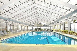 Ein Hallenbad mit hoher Decke, klaren Glasscheiben und Liegestühlen entlang der Seiten.