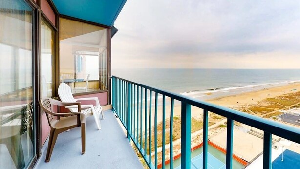 A balcony with a view of the beach and ocean, a table with chairs, and a blue railing. - Beachfront Condo w/Private Balcony, Telescope, Shared Pool, A/C, Free WiFi (Ocean City)
