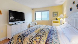 A bedroom with a bed, a TV, a chair, a window, and a bedside table. - Beachfront Condo w/Private Balcony, Telescope, Shared Pool, A/C, Free WiFi (Ocean City)