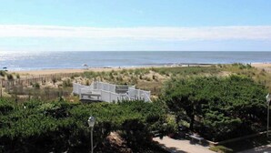 A beachfront property with a white building, sandy beach, and dense greenery. - Camelot 203B (Ocean City)