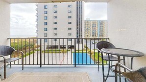 A balcony with a view of a swimming pool, a tall building, and a street. - Camelot 203B (Ocean City)
