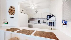 A kitchen with white cabinets, a white countertop, a ceiling fan, and a clock on the wall. - Camelot 203B (Ocean City)