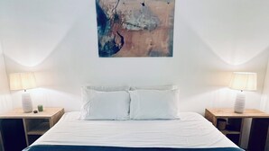 Quarto de hotel com uma cama grande, duas mesas de cabeceira, um quadro na parede e um tabuleiro sobre a cama.