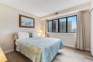 A hotel room with a bed, a window with curtains, a painting on the wall, and a lamp. - Coastal Condo w/Shared Pools, Gym, Private Balcony, Washer/Dryer, A/C, Free WiFi (Ocean City)