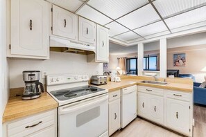 A compact kitchen with white cabinets, a stove, a coffee maker, and a sink. - Coastal Condo w/Shared Pools, Gym, Private Balcony, Washer/Dryer, A/C, Free WiFi (Ocean City)