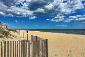 Ein Strand mit einer Holzumzäunung, sandigem Ufer und Gebäuden im Hintergrund.