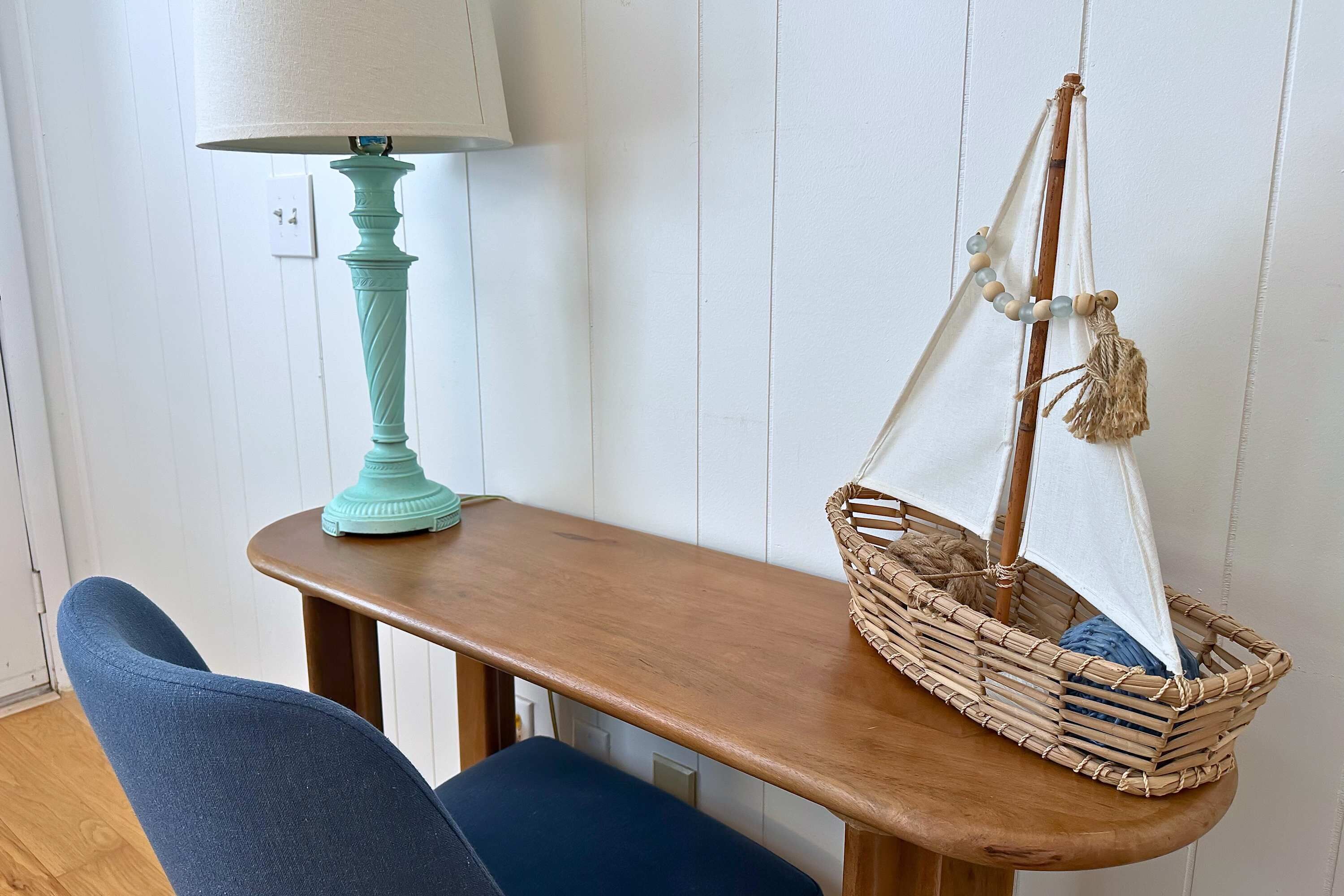 A wooden table with a lamp and a wicker basket with a sail.