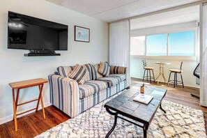 A living room with a sofa, a coffee table, a TV, and a balcony with chairs. - Fun-Filled Vacation Condo in Beachfront Complex w/Shared Pool, Free WiFi (Ocean City)
