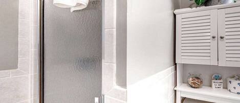 A bathroom with a shower, a toilet, a cabinet with a plant, and a welcome sign.