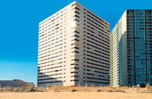 A tall, modern building with a flat facade and numerous windows, situated on a sandy area with a clear blue sky. - Fun-Filled Vacation Condo in Beachfront Complex w/Shared Pool, Free WiFi (Ocean City)
