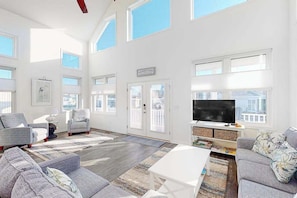 A spacious living room with a large TV, multiple seating areas, and large windows. - Atlantic Blvd 13314 (Ocean City)