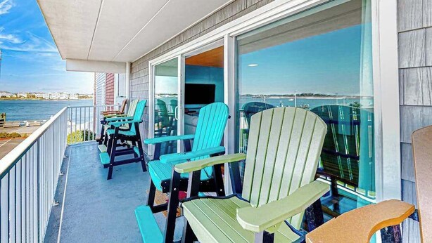 A balcony with Adirondack chairs, a table, and a view of the water. - Assateague House 205 (Ocean City)
