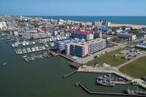 An aerial view of a coastal town with a marina, buildings with red roofs, and a beach in the background. - Assateague House 205 (Ocean City)
