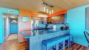 A kitchen with a central island, bar stools, and a view into the adjacent dining area. - Assateague House 205 (Ocean City)