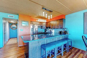 A kitchen with a central island, bar stools, and a view into the adjacent dining area. - Assateague House 205 (Ocean City)
