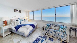 Un dormitorio con una ventana grande, una cama, una mesita de noche, una silla y un cartel en la pared.