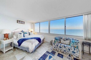 A bedroom with a large window, a bed, a nightstand, a chair, and a wall sign. - Antigua 1004 (Ocean City)