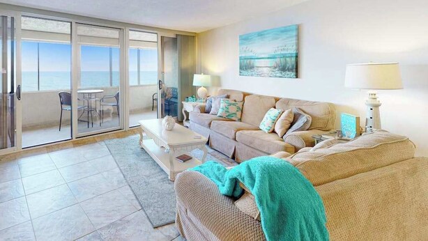 Una sala de estar con sofá, mesa de centro y vista al mar a través de una puerta corrediza de vidrio.